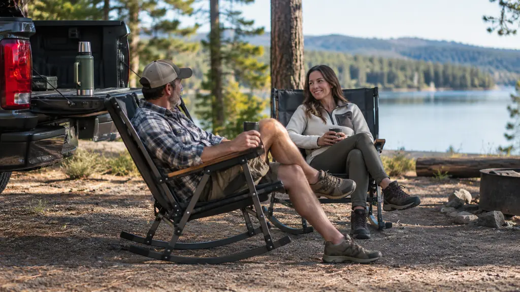 Two folding rocking camp chairs set up side by side beside a pickup truck tailgate at a campground in the morning