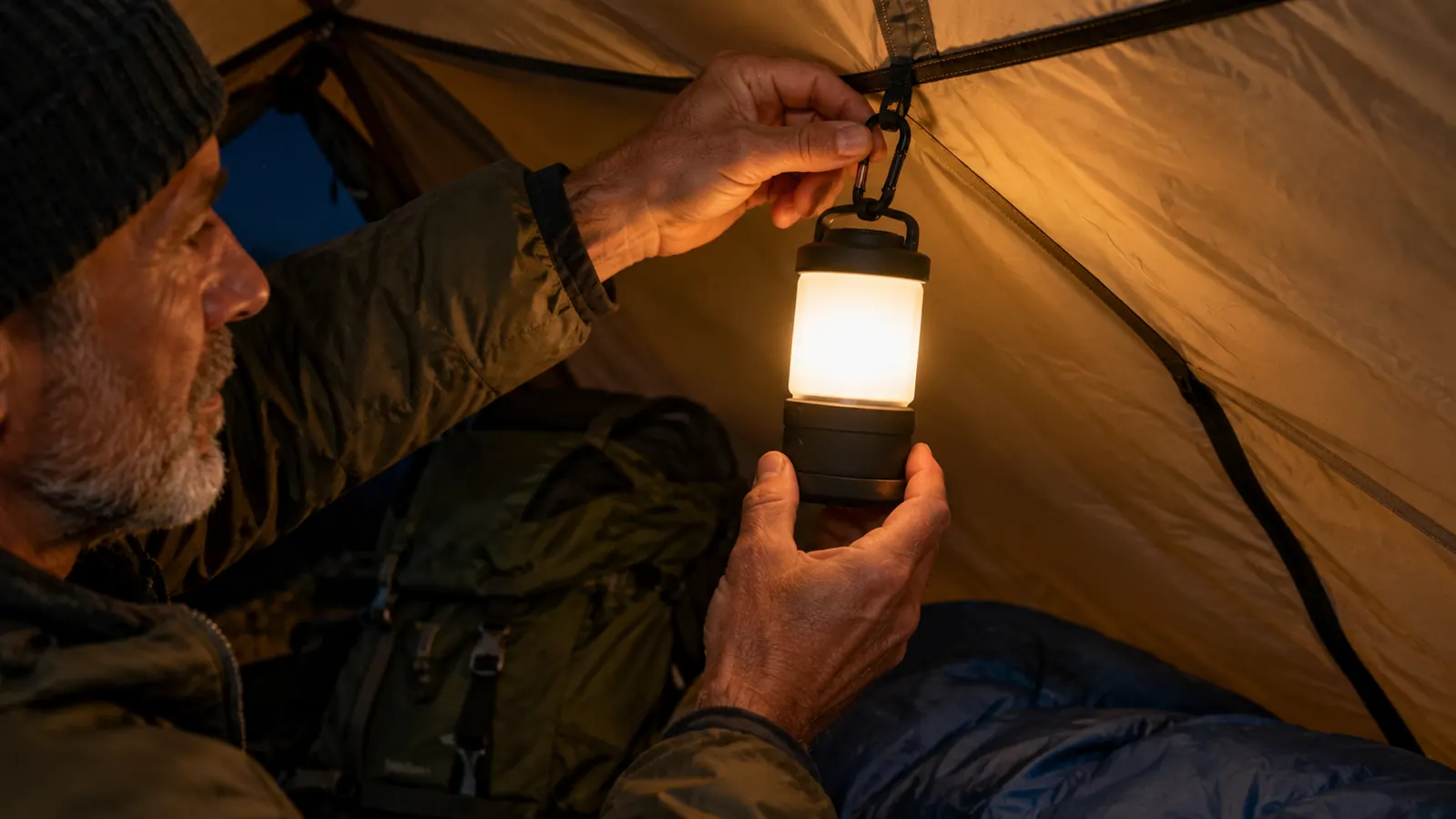 A hand hanging a lantern from a hook inside a tent at night